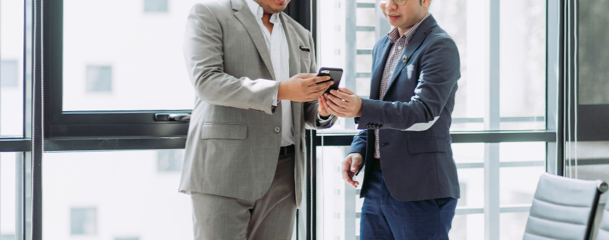 person holding phone and showing it to another person standing next to them